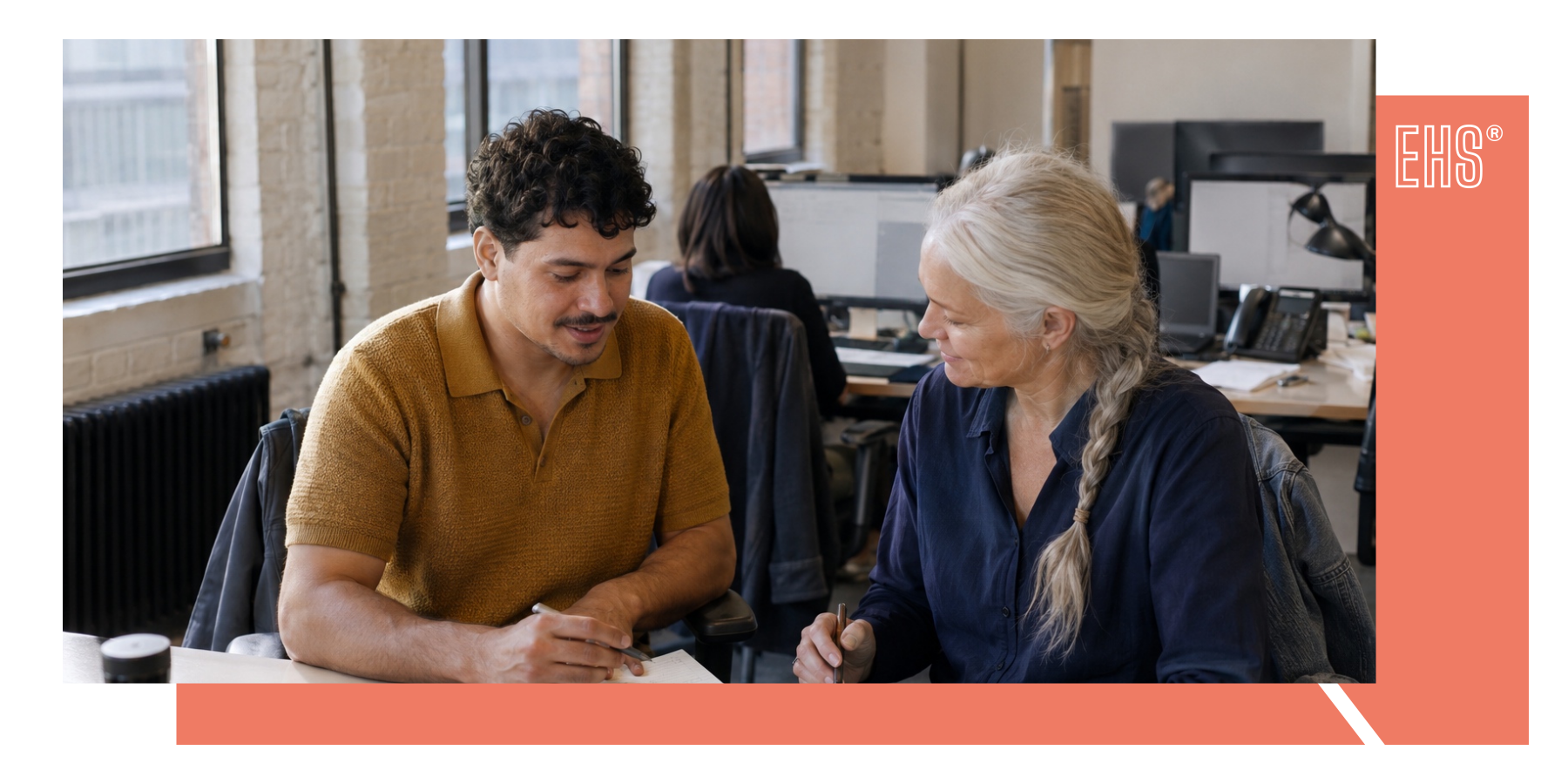 Two colleagues comparing notes at a desk with EHS branding